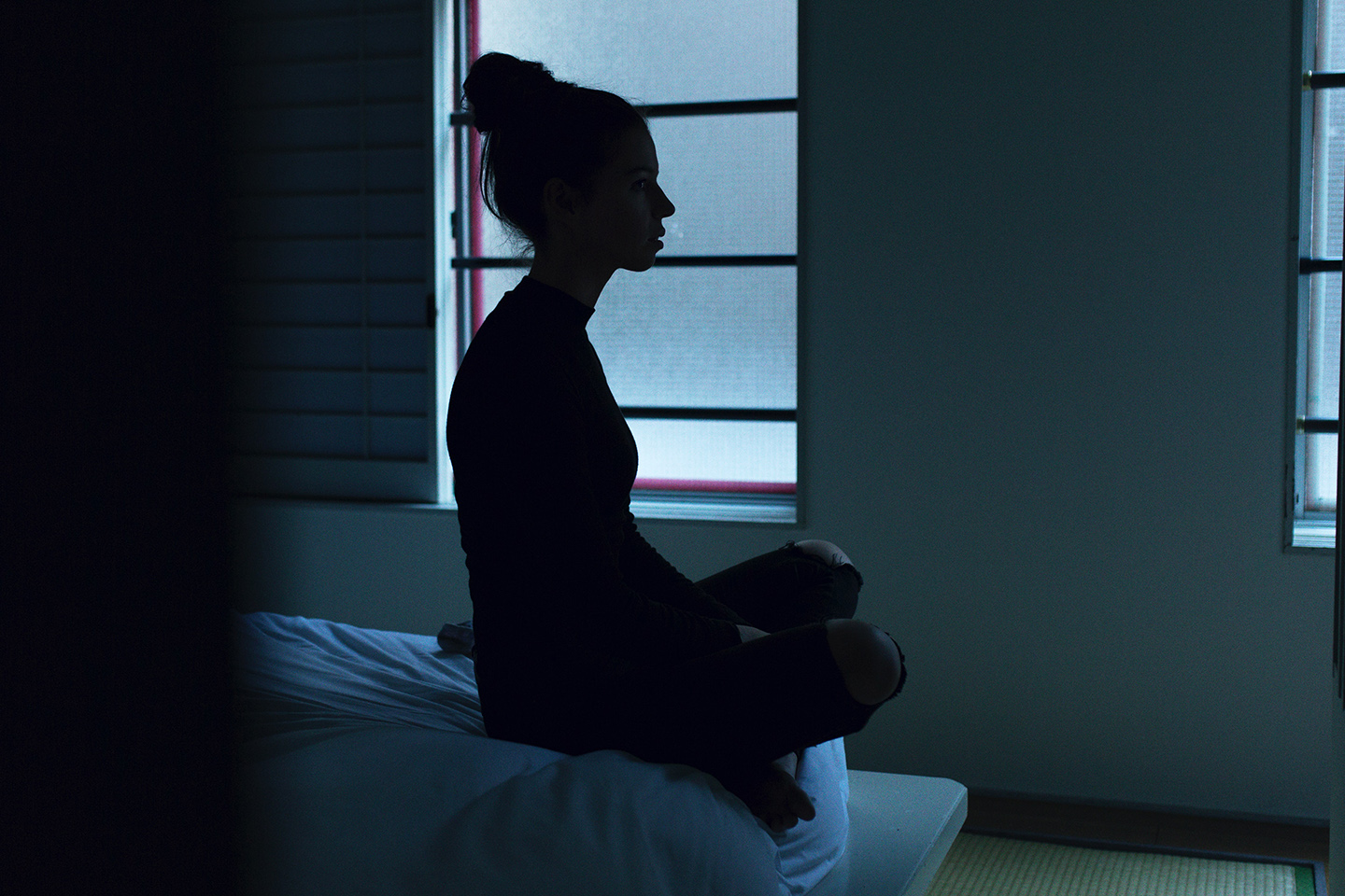 Woman sitting on end of bed in the dark at dusk